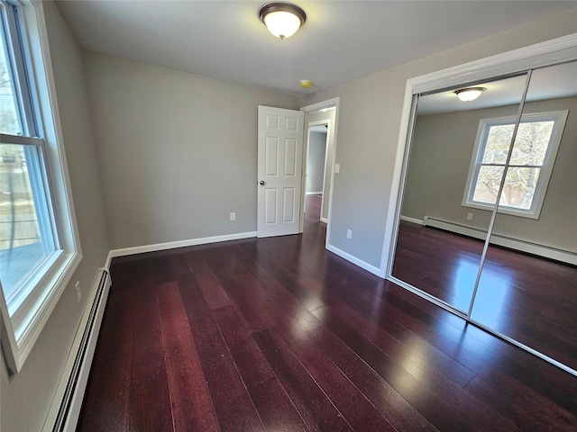 unfurnished bedroom featuring a closet, wood finished floors, baseboards, and baseboard heating