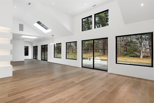 unfurnished living room with visible vents, recessed lighting, light wood-style floors, a skylight, and high vaulted ceiling