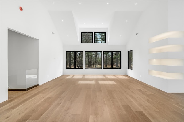 unfurnished living room with recessed lighting, a high ceiling, and light wood-style flooring