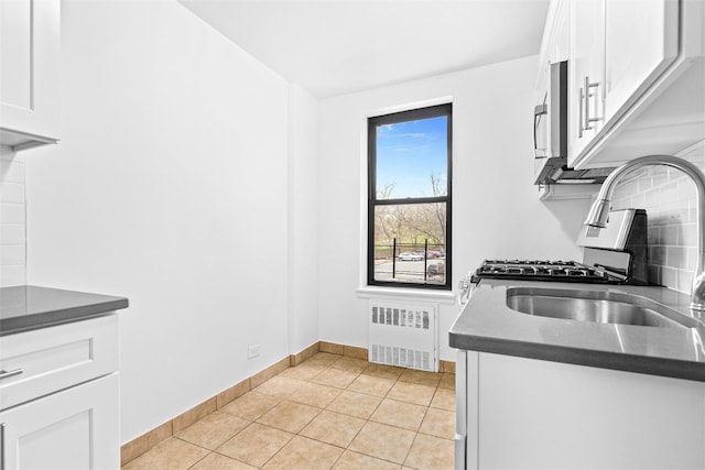 kitchen featuring dark countertops, radiator heating unit, white cabinetry, and light tile patterned floors