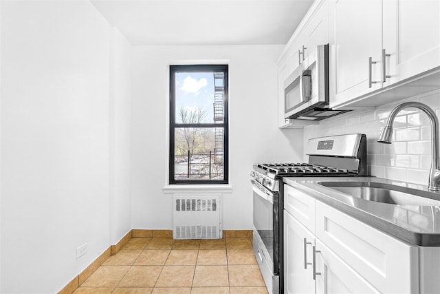 kitchen featuring a sink, stainless steel appliances, tasteful backsplash, radiator heating unit, and white cabinetry