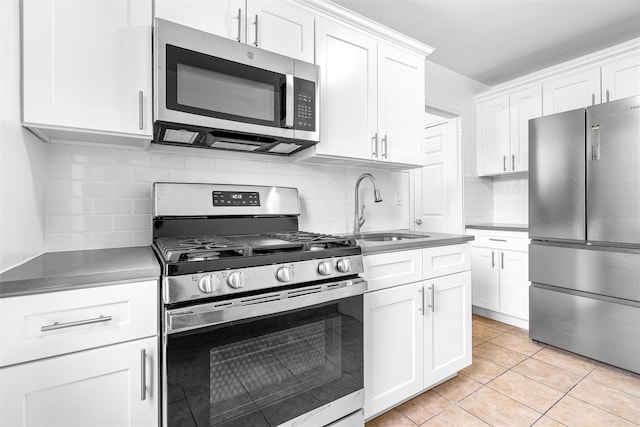 kitchen featuring light tile patterned floors, tasteful backsplash, white cabinets, a sink, and stainless steel appliances