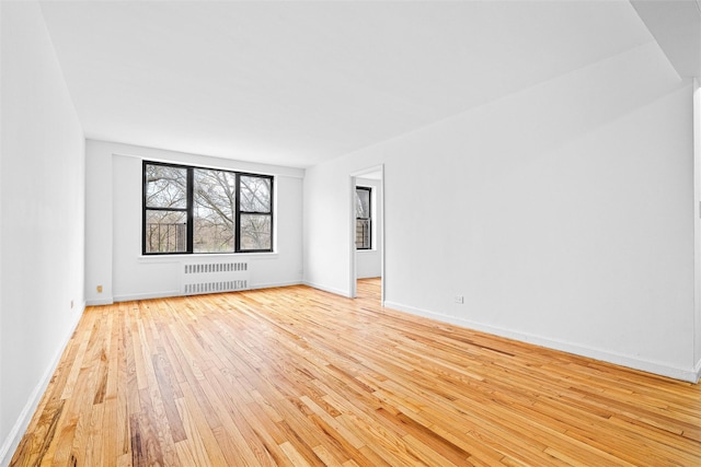 spare room with baseboards, radiator, and light wood-style floors