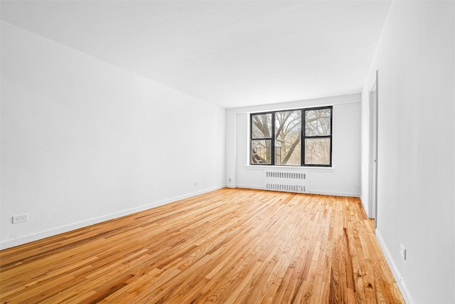 spare room with baseboards, radiator, and light wood finished floors