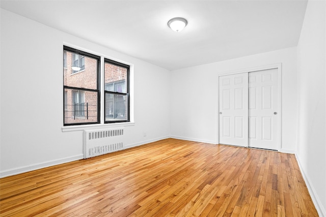 unfurnished bedroom featuring radiator heating unit, light wood-type flooring, a closet, and baseboards
