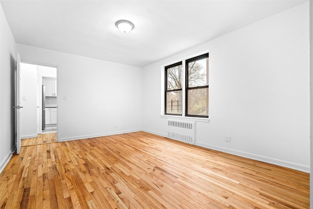 unfurnished bedroom featuring baseboards, radiator heating unit, and light wood-type flooring