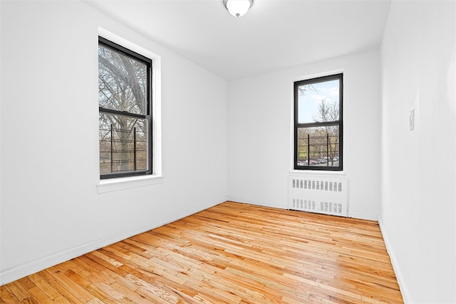 unfurnished room featuring hardwood / wood-style floors, baseboards, and radiator