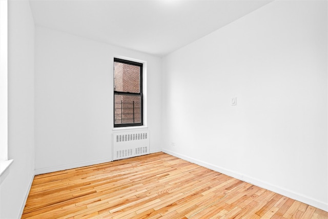 unfurnished room featuring radiator, hardwood / wood-style flooring, and baseboards