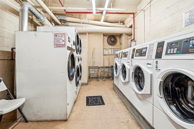 community laundry room with concrete block wall, stacked washer / drying machine, light tile patterned flooring, and independent washer and dryer