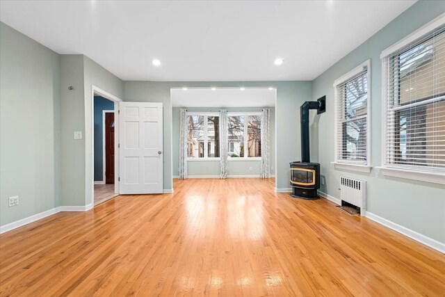 89-21 Aubrey Ave, Glendale, NY 11385 - unfurnished living room with radiator, a wood stove, light wood-style flooring, baseboards, and recessed lighting