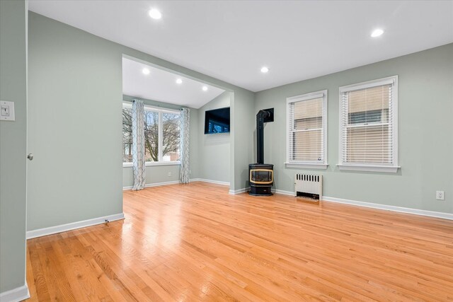 89-21 Aubrey Ave, Glendale, NY 11385 - unfurnished living room featuring radiator, a wood stove, light wood-style flooring, baseboards, and recessed lighting