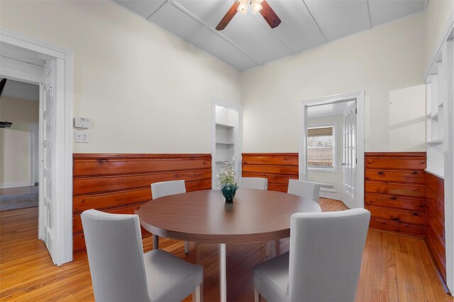 dining area featuring a wainscoted wall, wooden walls, ceiling fan, and light wood finished floors