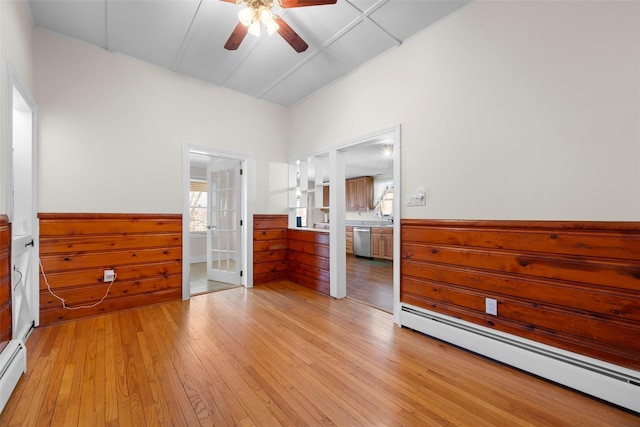 unfurnished bedroom featuring a baseboard heating unit, light wood-style floors, a wainscoted wall, and wooden walls