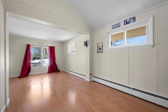 empty room featuring a baseboard heating unit, lofted ceiling, wood finished floors, and baseboards
