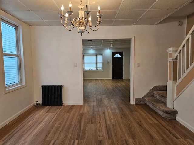 unfurnished dining area featuring stairway, radiator heating unit, wood finished floors, a notable chandelier, and a paneled ceiling