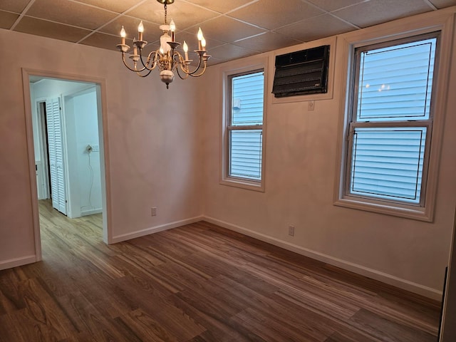 empty room with a chandelier, a paneled ceiling, dark wood-type flooring, and baseboards