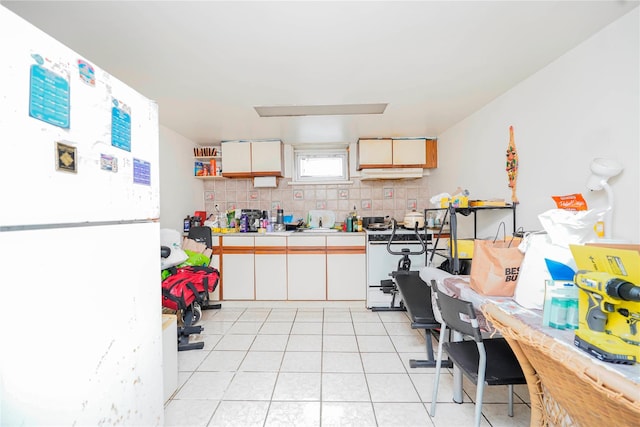 kitchen with light tile patterned floors, freestanding refrigerator, tile counters, under cabinet range hood, and backsplash