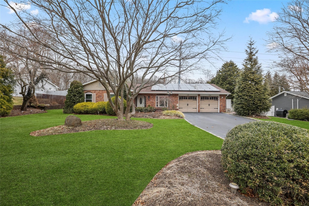 ranch-style home featuring driveway, roof mounted solar panels, an attached garage, a front yard, and brick siding
