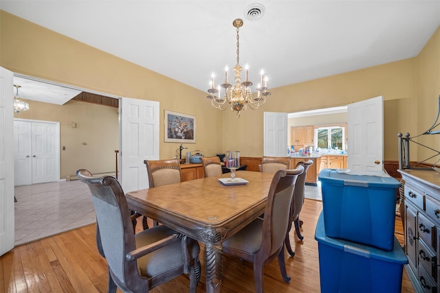 dining space featuring light wood-type flooring, visible vents, and a chandelier