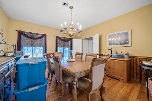 dining room featuring wood walls, an inviting chandelier, a wainscoted wall, visible vents, and light wood-style flooring