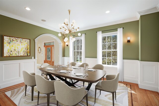 dining area with arched walkways, a notable chandelier, wainscoting, and a decorative wall