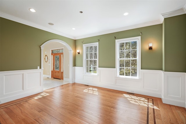spare room featuring crown molding, visible vents, a wainscoted wall, arched walkways, and light wood-style flooring