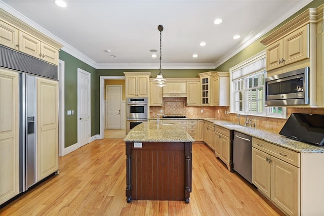 kitchen with built in appliances, an island with sink, light stone counters, a sink, and light wood finished floors