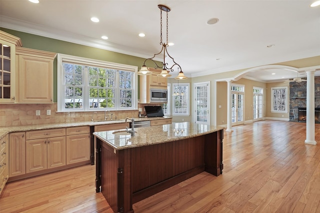 kitchen featuring ornamental molding, decorative columns, open floor plan, stainless steel microwave, and a sink