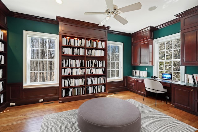 office space featuring crown molding, ceiling fan, built in study area, light wood-type flooring, and visible vents