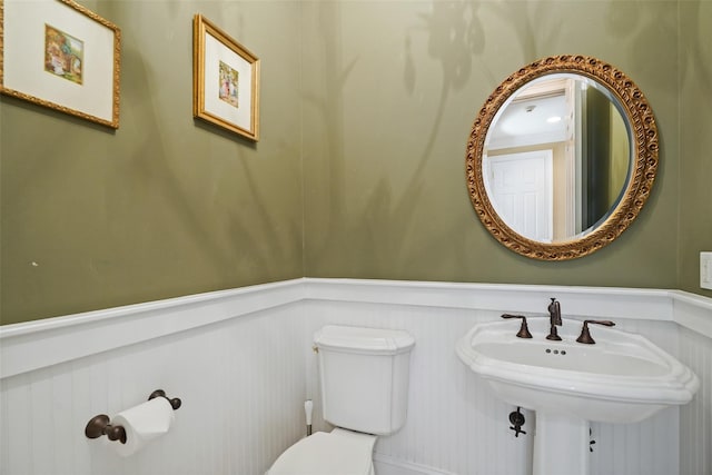 half bath featuring toilet, a sink, a wainscoted wall, and a decorative wall