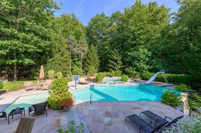 pool featuring a patio, a water slide, a wooded view, and an outdoor hangout area