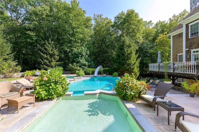 view of pool featuring a deck, a pool with connected hot tub, a water slide, and a patio area