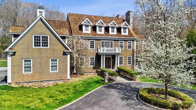 view of front of property featuring a chimney, a balcony, and a front yard