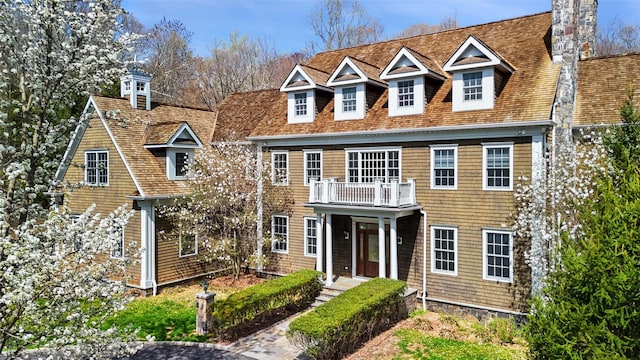 view of front of house with roof with shingles, a chimney, and a balcony