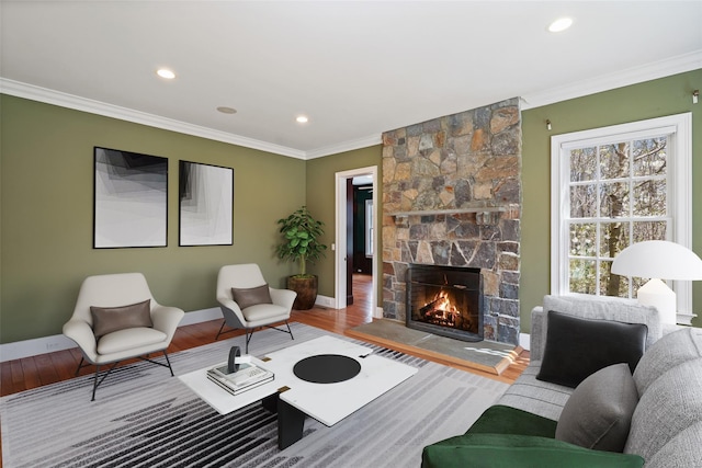 living room with ornamental molding, wood finished floors, a stone fireplace, baseboards, and recessed lighting