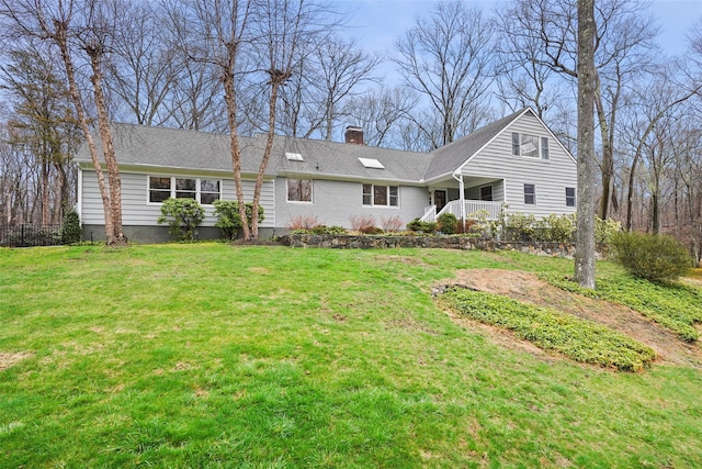rear view of house with a shingled roof, covered porch, a lawn, and a chimney