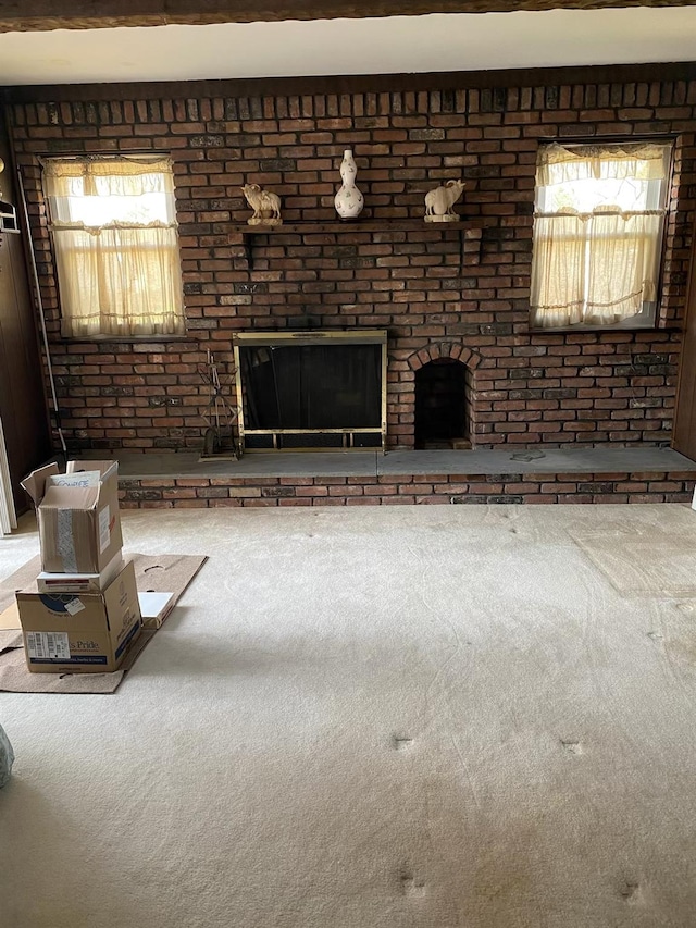 unfurnished living room featuring carpet flooring, brick wall, a healthy amount of sunlight, and a fireplace