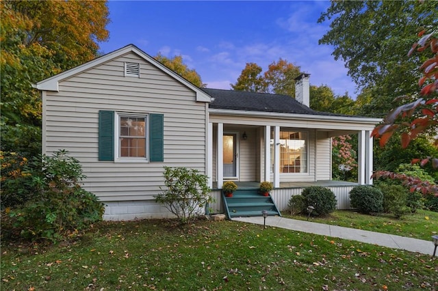 view of front of house with a porch, a chimney, a front yard, and a shingled roof