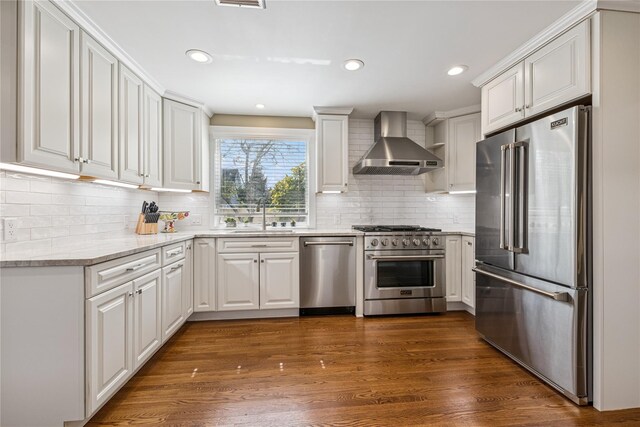 kitchen featuring a sink, wall chimney exhaust hood, premium appliances, white cabinets, and dark wood-type flooring