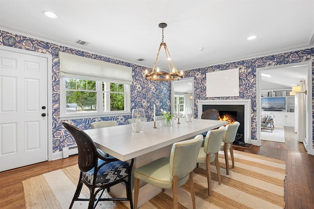 dining room featuring dark wood-style flooring, a baseboard radiator, ornamental molding, and wallpapered walls