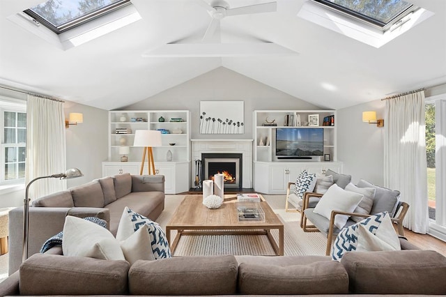 living room featuring vaulted ceiling with skylight, a ceiling fan, a lit fireplace, and wood finished floors