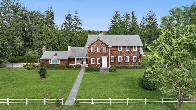 colonial inspired home featuring a shingled roof, a front lawn, fence, and a chimney