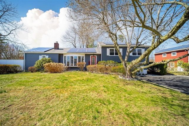 tri-level home featuring a chimney, a front lawn, and roof mounted solar panels