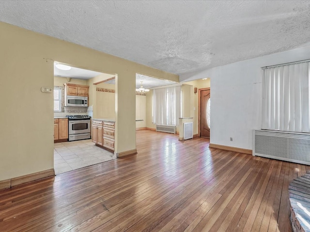 unfurnished living room with light wood finished floors, a notable chandelier, a textured ceiling, and radiator heating unit