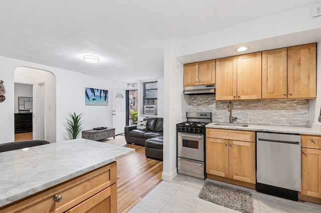 kitchen with arched walkways, a sink, tasteful backsplash, under cabinet range hood, and appliances with stainless steel finishes