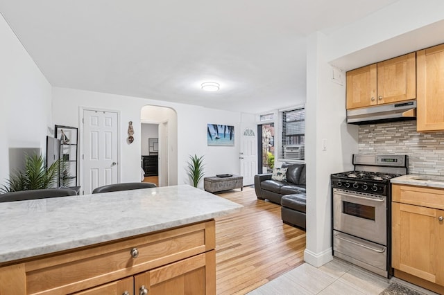 kitchen featuring tasteful backsplash, open floor plan, arched walkways, stainless steel gas stove, and under cabinet range hood