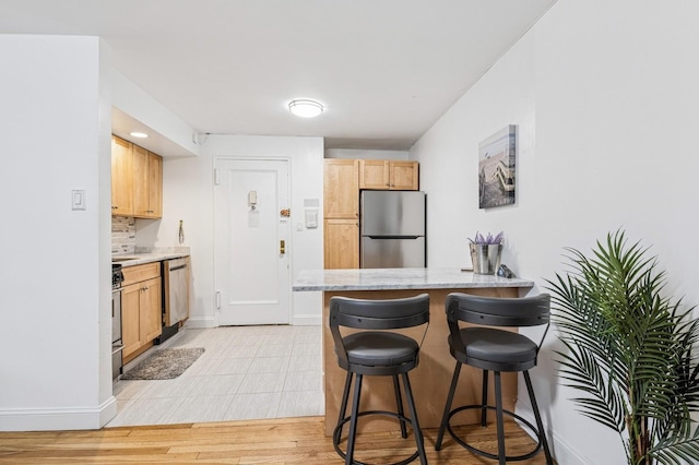 kitchen featuring light brown cabinetry, a kitchen breakfast bar, light stone countertops, a peninsula, and appliances with stainless steel finishes