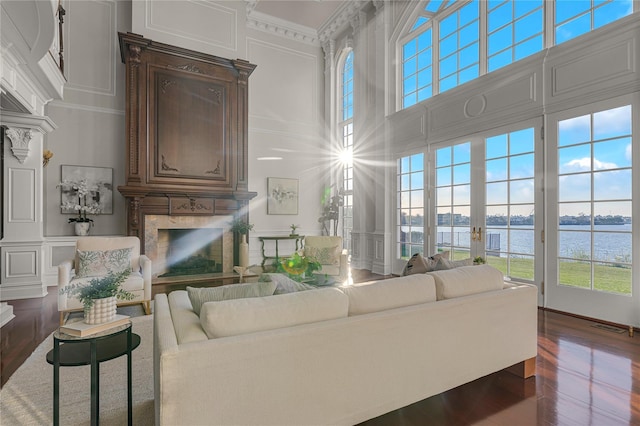 living area with a decorative wall, a high end fireplace, a towering ceiling, a water view, and dark wood-type flooring