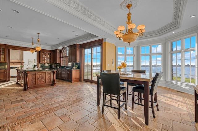 dining space with a chandelier, ornamental molding, stone tile floors, a water view, and a tray ceiling