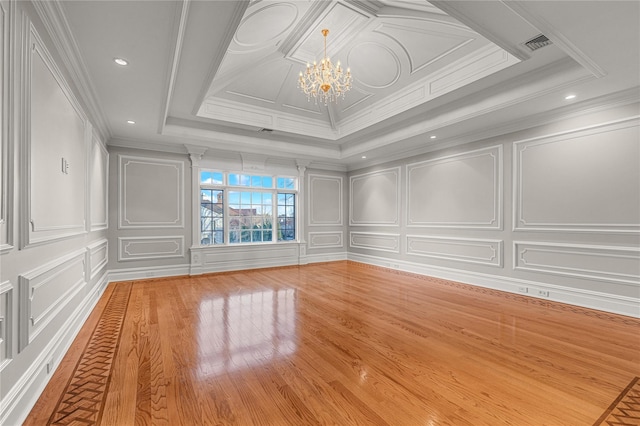 spare room with a decorative wall, a chandelier, wood finished floors, crown molding, and a raised ceiling